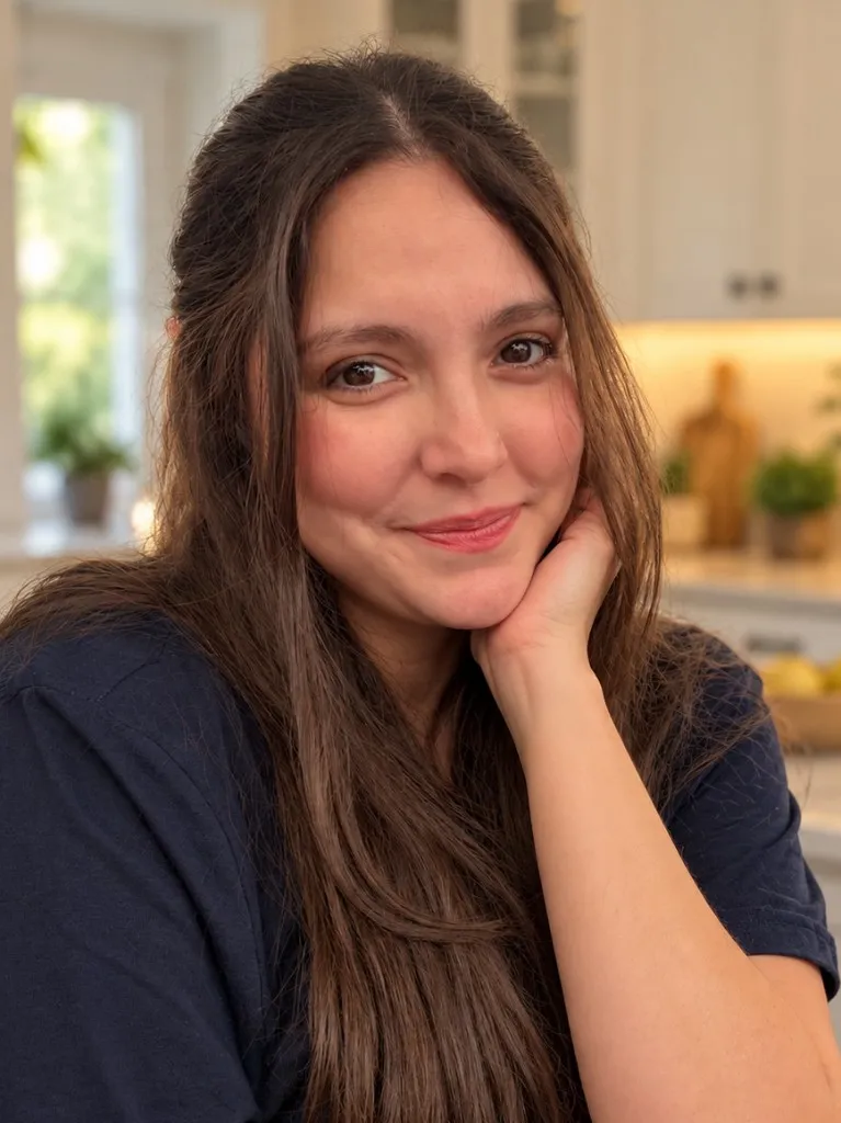 Ashley Art in her kitchen, wearing a navy shirt, chin resting on her hand.
