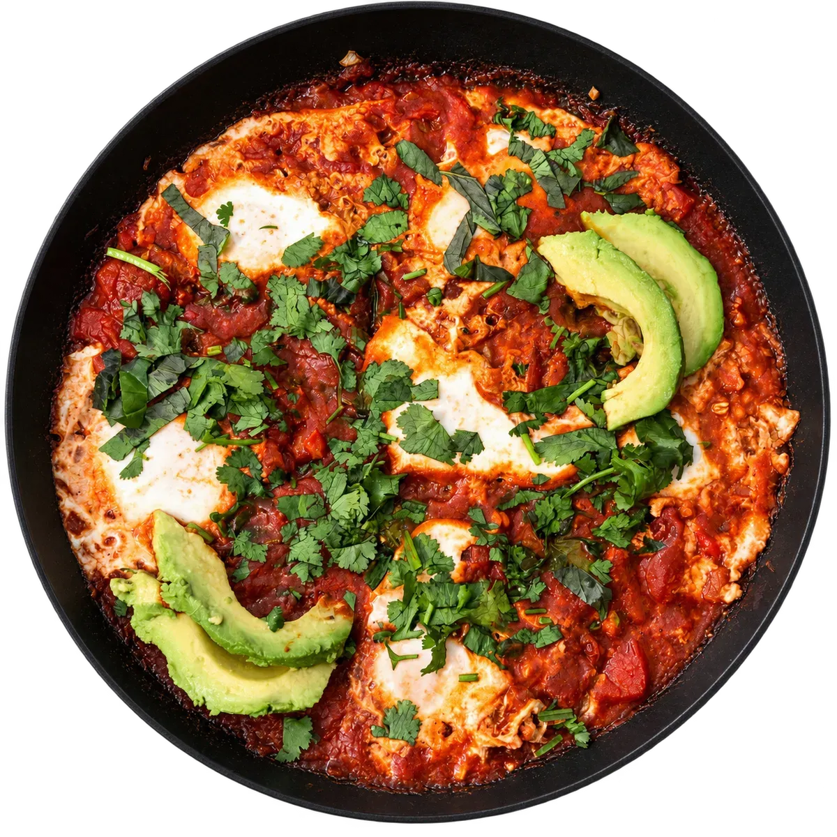 Shakshuka in a skillet with eggs, tomato sauce, avocado, and herbs.